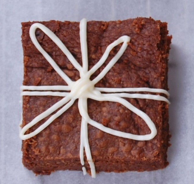 Brownie square topped with white icing piped into a six-point star/flower on parchment paper.