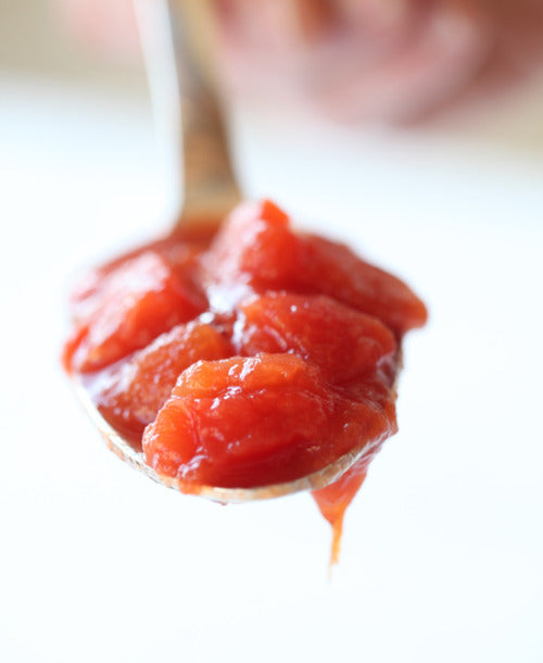 Spoonful of peeled plum tomatoes in tomato sauce with a drip