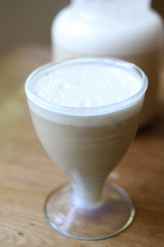 Horchata a creamy beige, frothy drink in a stemmed glass on a wooden surface