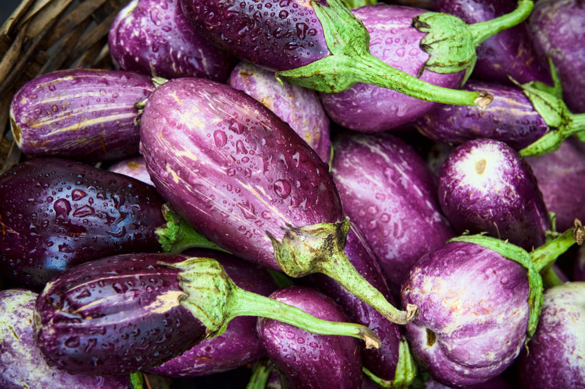 Variegated purple eggplants with water droplets in a woven basket