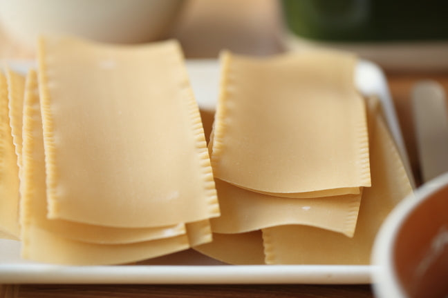 Uncooked lasagna sheets stacked on a white plate, close-up