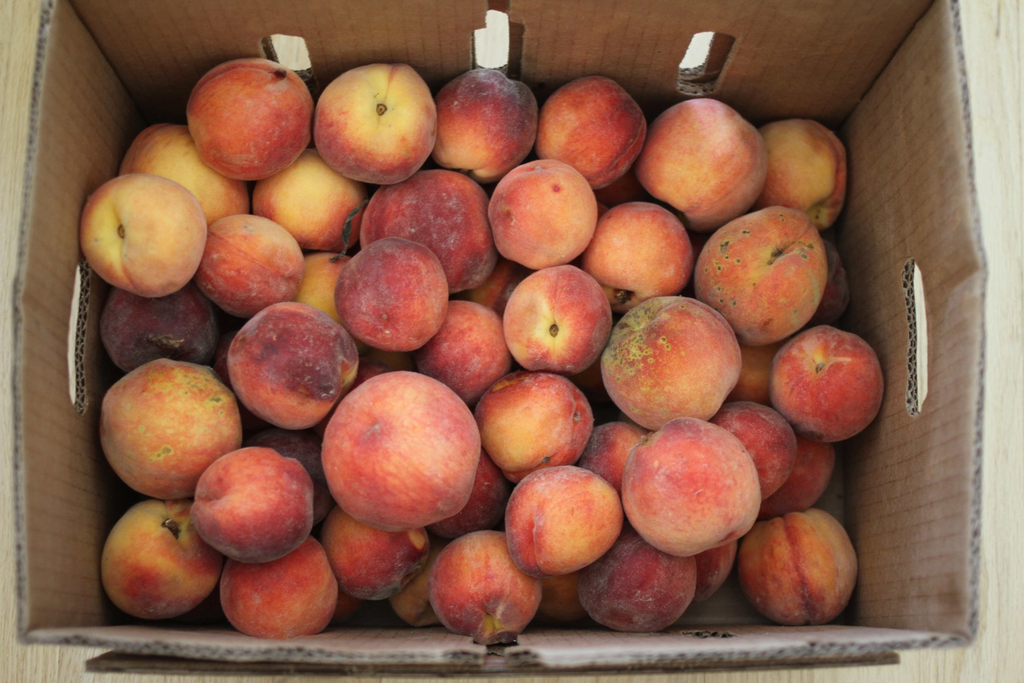 Cardboard box of ripe peaches with red-orange fuzzy skins
