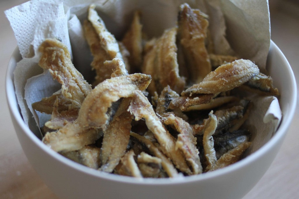 Bowl of crispy fried anchovies on a paper towel-lined bowl.