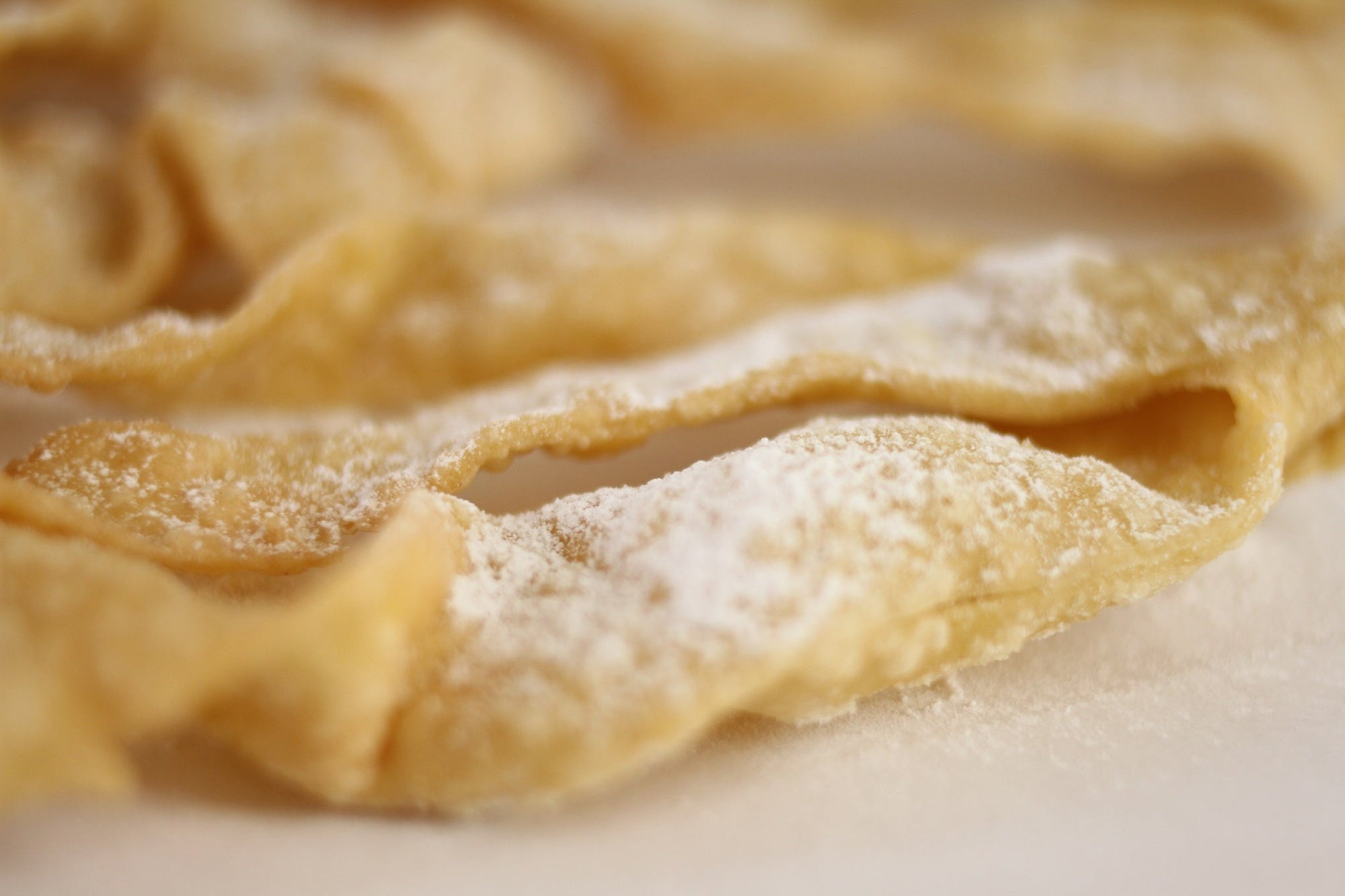 Close-up of Italian frappe (cenci) showcasing thin twisted ribbons dusted with powdered sugar on parchment paper