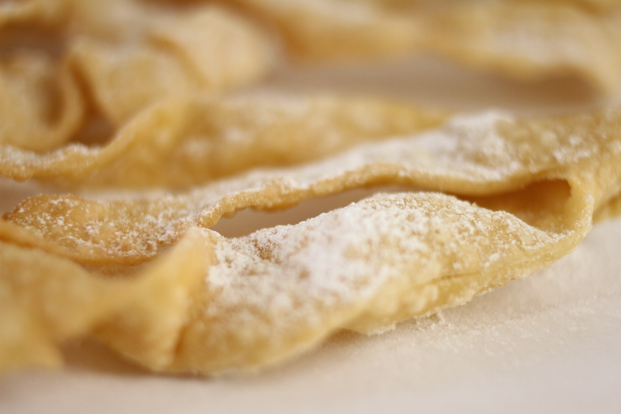 Close-up of Italian frappe (cenci) showcasing thin twisted ribbons dusted with powdered sugar on parchment paper