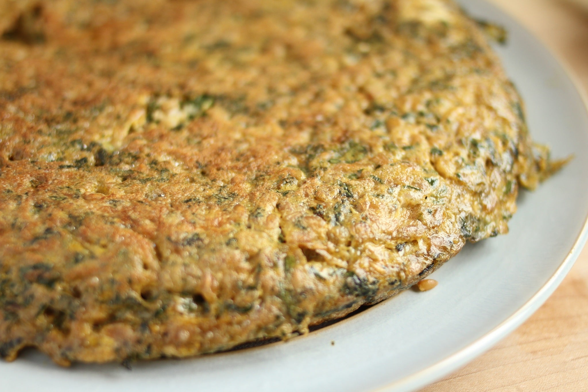 Golden-brown herb and spinach frittata on a white plate