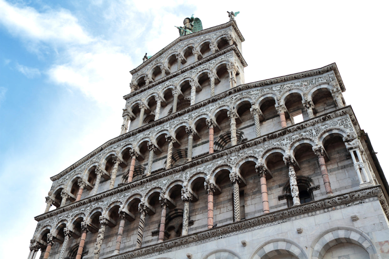 Romanesque cathedral facade with multiple stacked arcades, carved columns, and statues against a blue sky