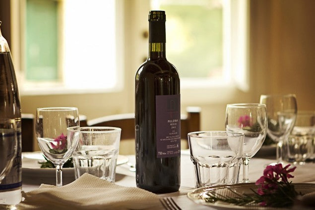 Bottle of red wine centered on a set dining table with wine and water glasses, napkin, and pink flowers