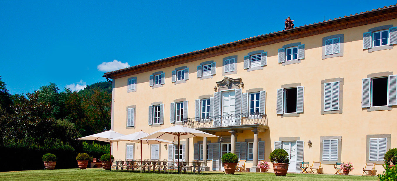 Sunlit Italian villa with shuttered windows, umbrellas and outdoor tables on a manicured lawn