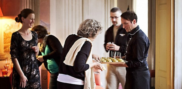 Server offering a tray of hors d'oeuvres to guests at a small, warm indoor gathering.