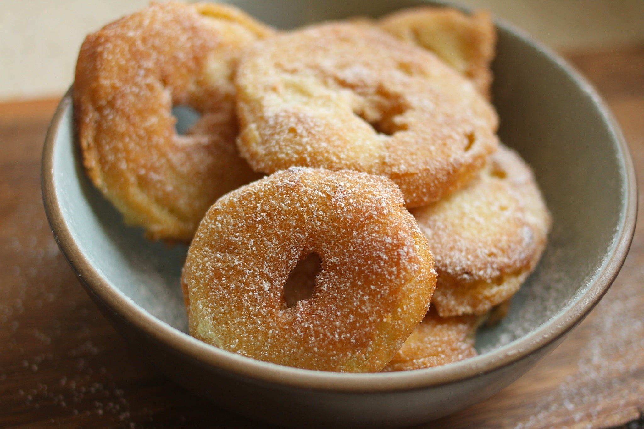 Sugar-dusted fried apple rings stacked in a gray bowl on a wooden board