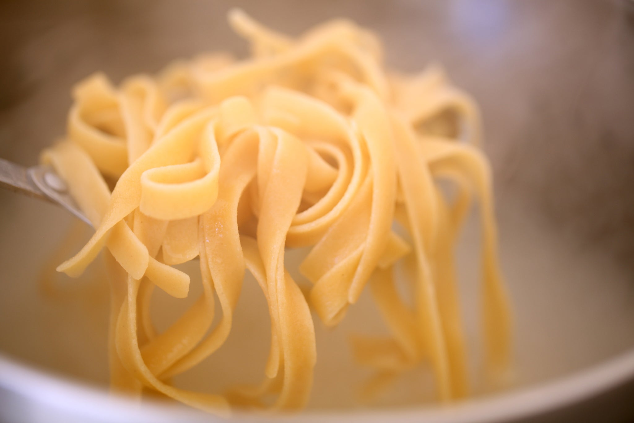 Fork lifting fresh tagliatelle-style pasta strands above cooking water