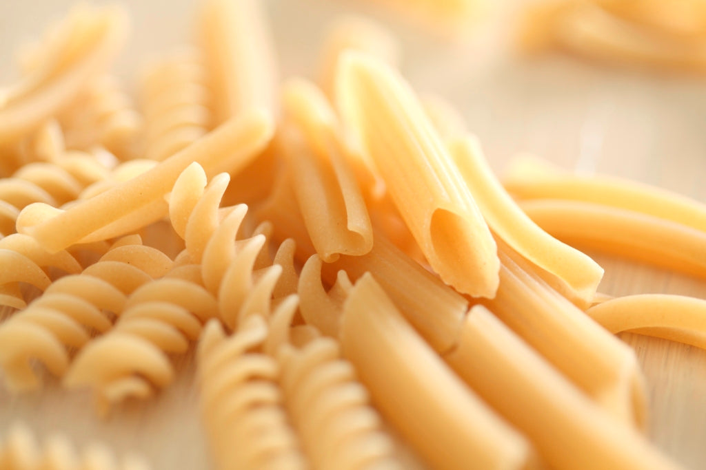 Uncooked penne and fusilli pasta scattered on a wooden surface