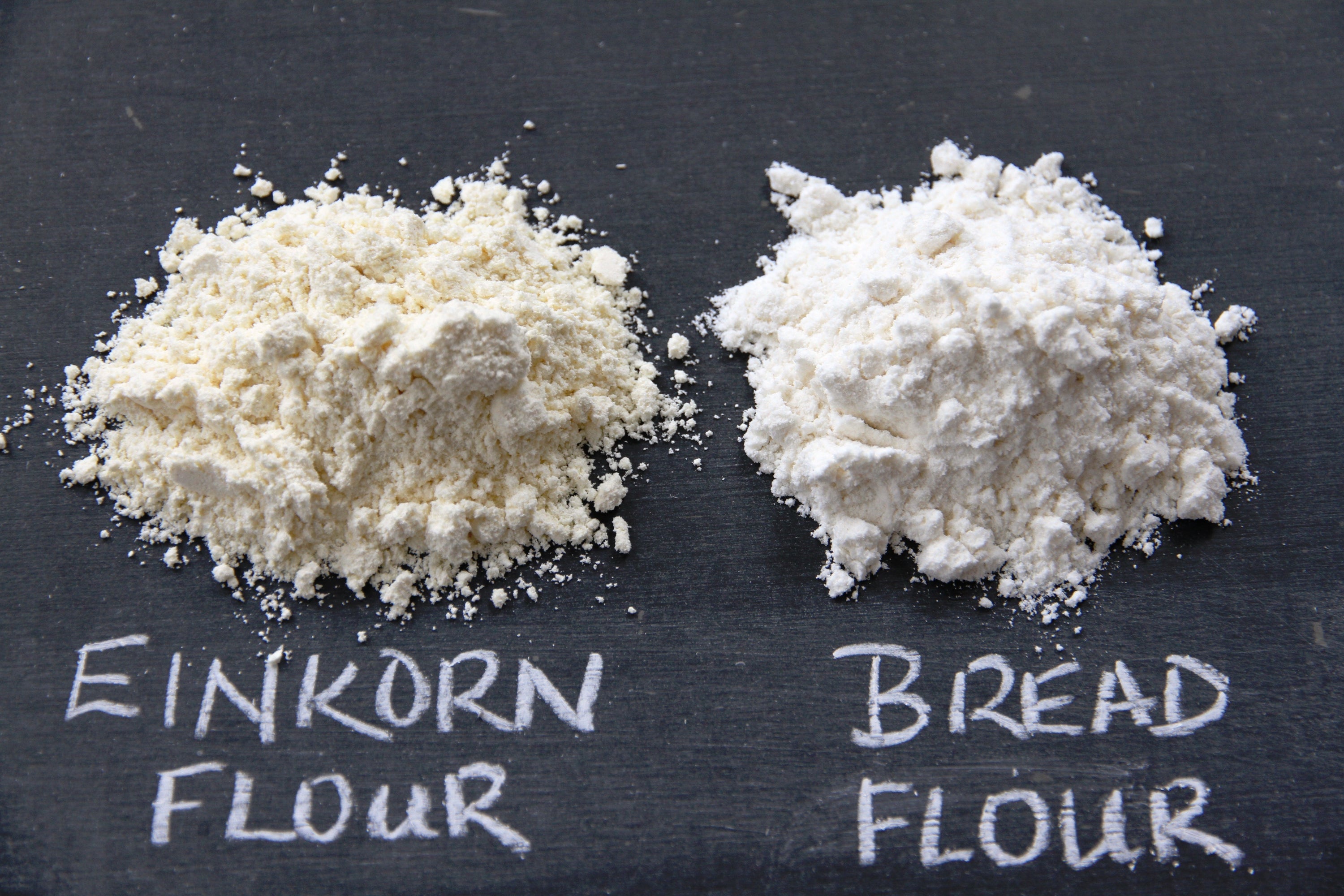 Two flour piles on chalkboard labeled 'EINKORN FLOUR' (left) and 'BREAD FLOUR' (right)