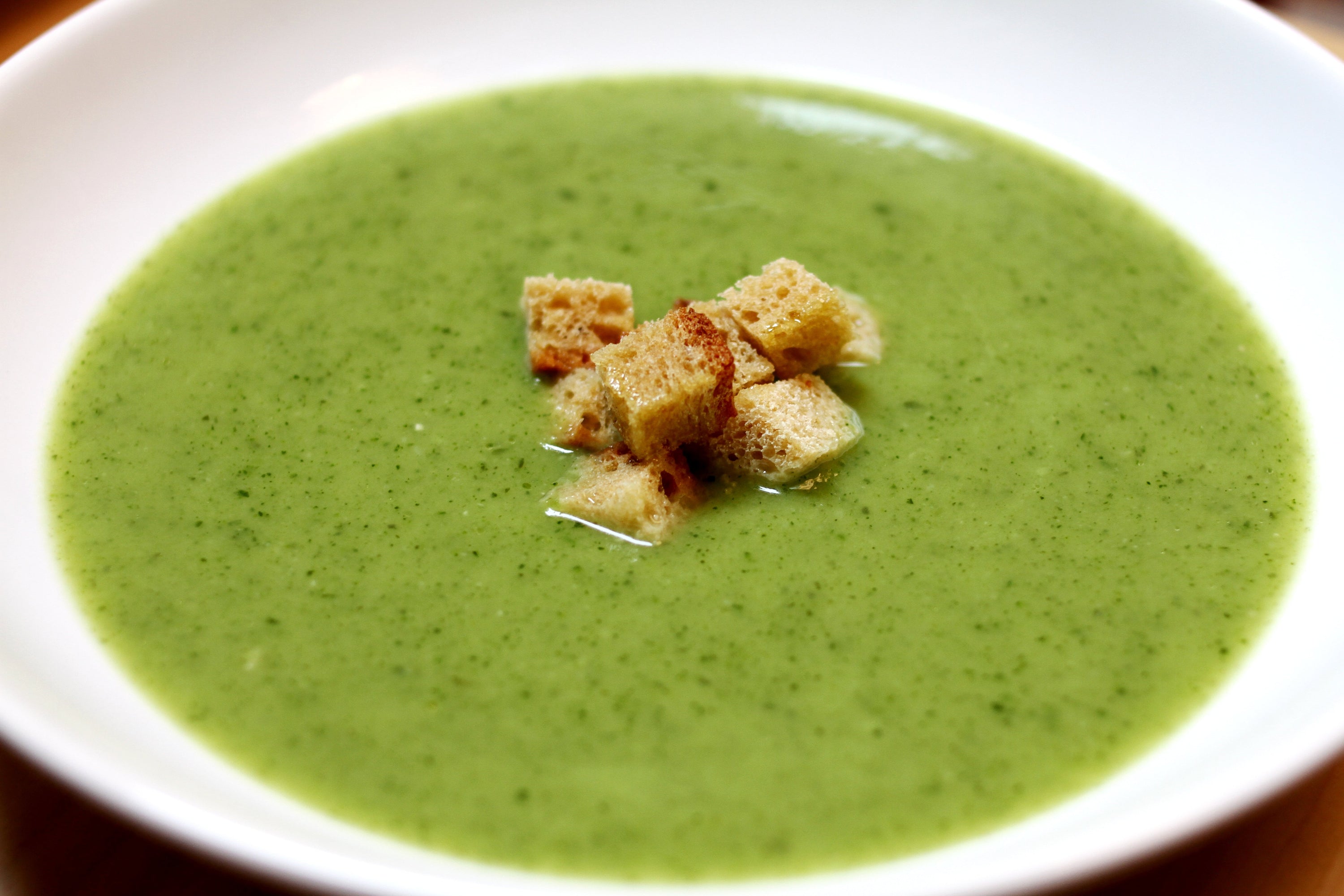 Creamy green soup with cubed croutons in a white bowl