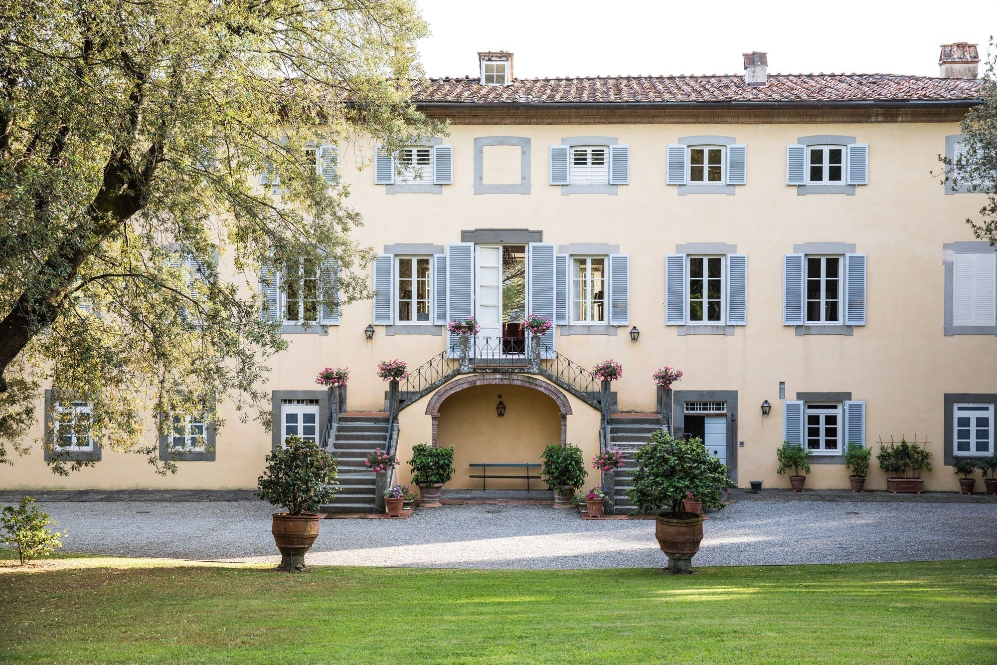Courtyard of Italian villa with blue shutters, double stone staircase, potted flowers and bench — Jovial culinary getaway