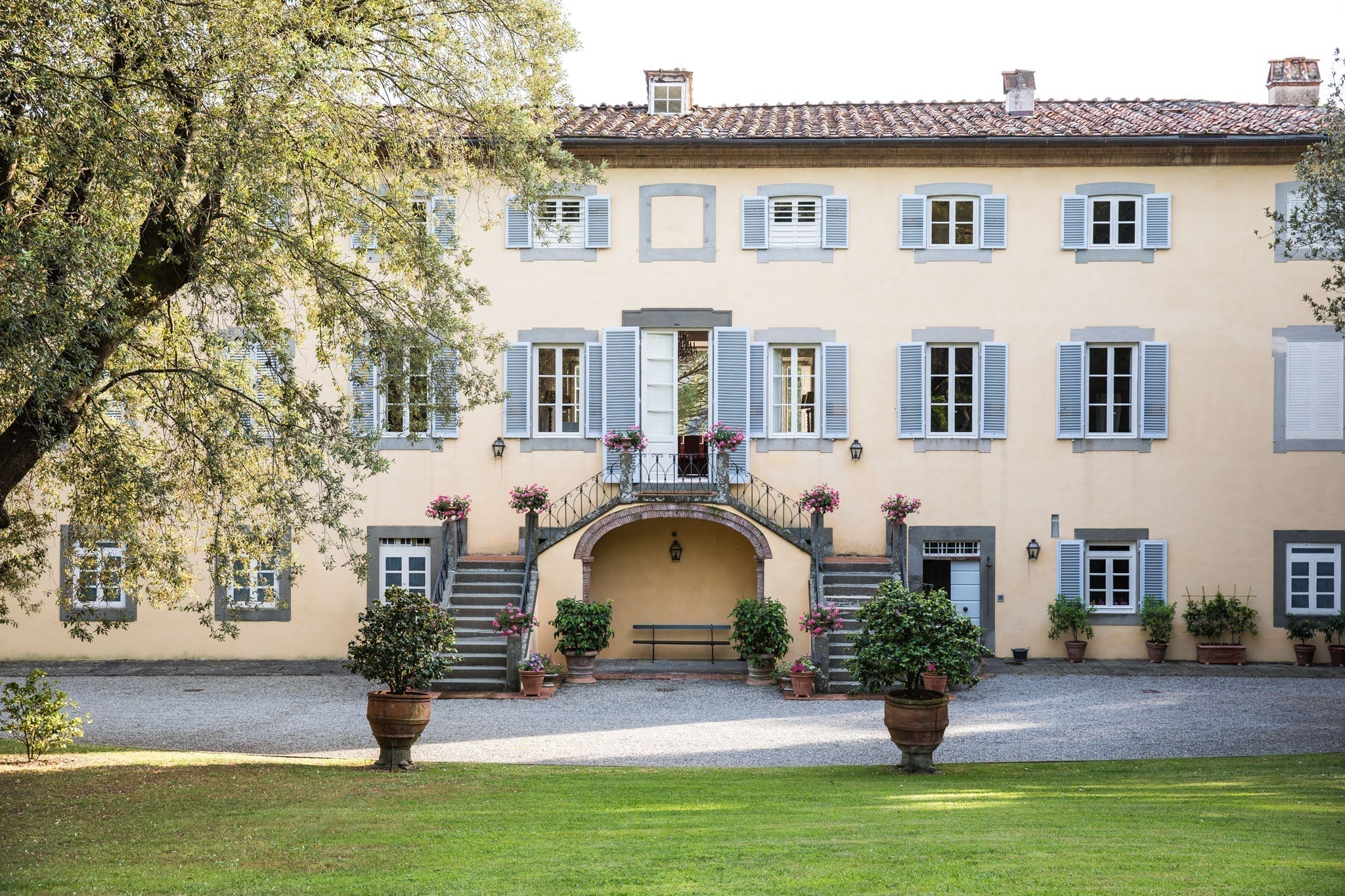 Courtyard of Italian villa with blue shutters, double stone staircase, potted flowers and bench — Jovial culinary getaway