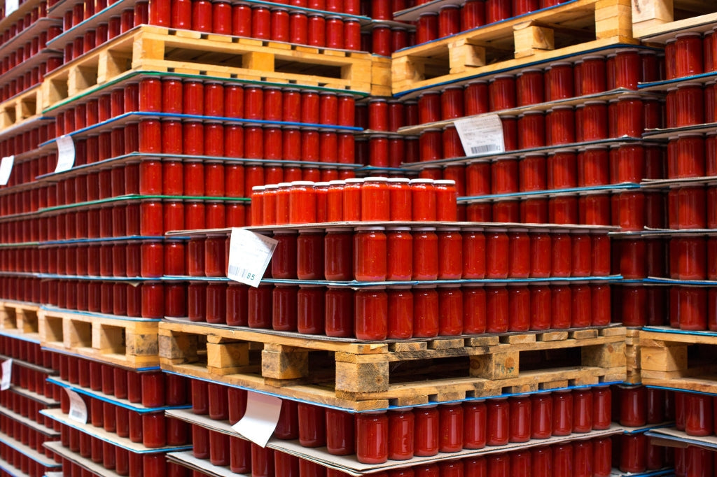 Rows of red tomato-sauce jars on wooden pallets in a warehouse storage area
