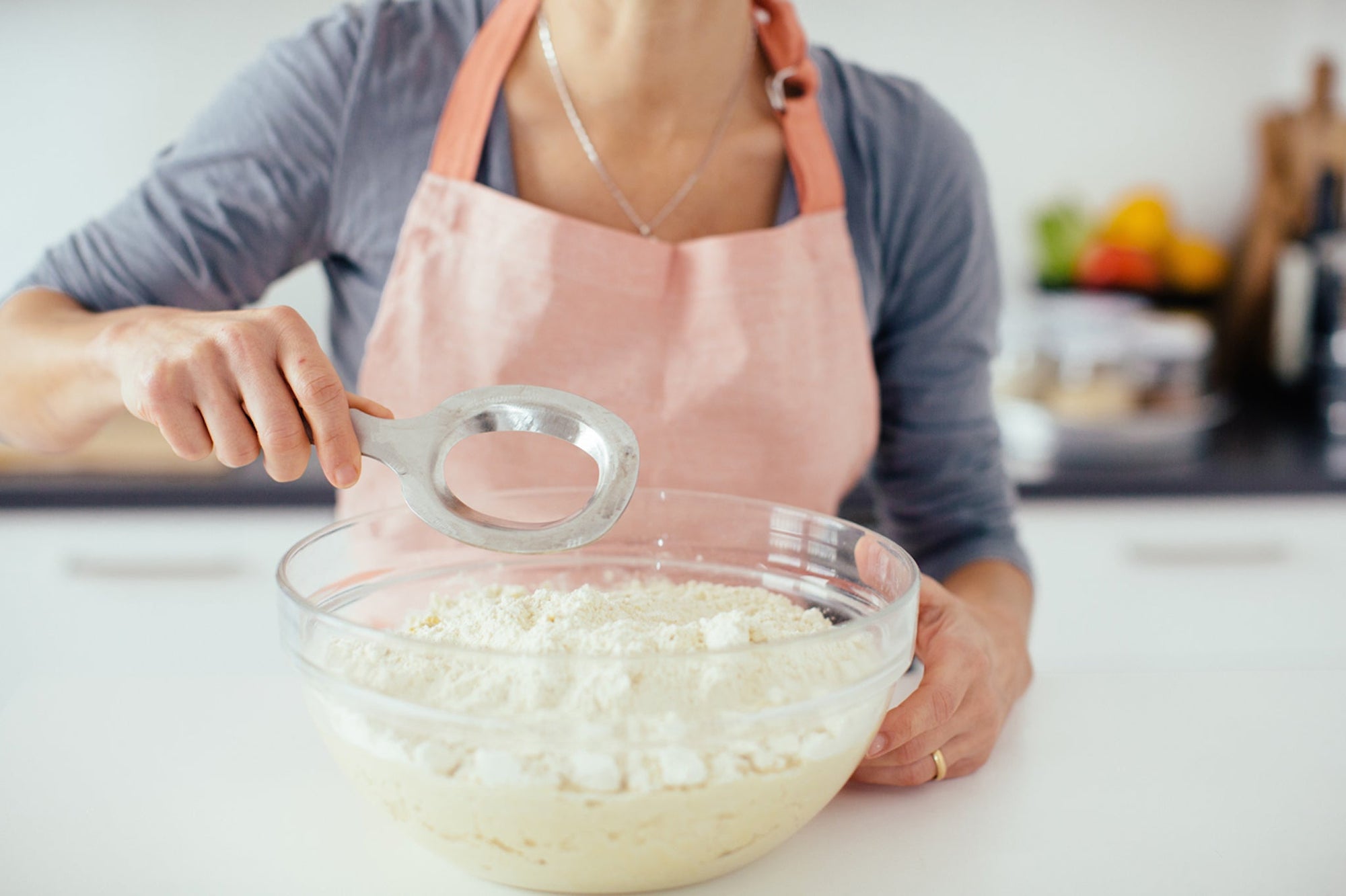 Person in pink apron using a metal dough blender to mix flour and dough in a glass bowl.