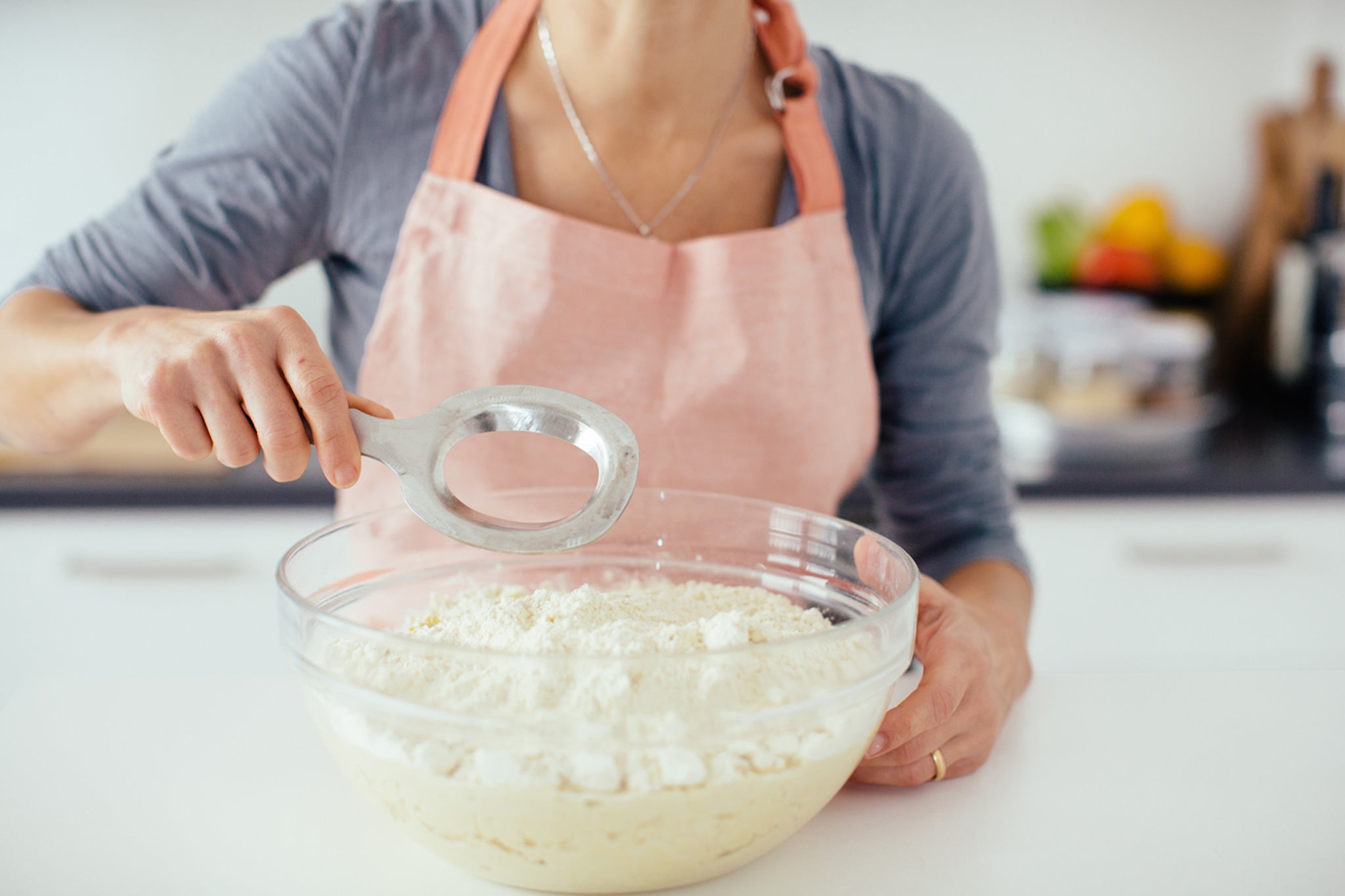 Person in pink apron using a metal dough blender to mix flour and dough in a glass bowl.