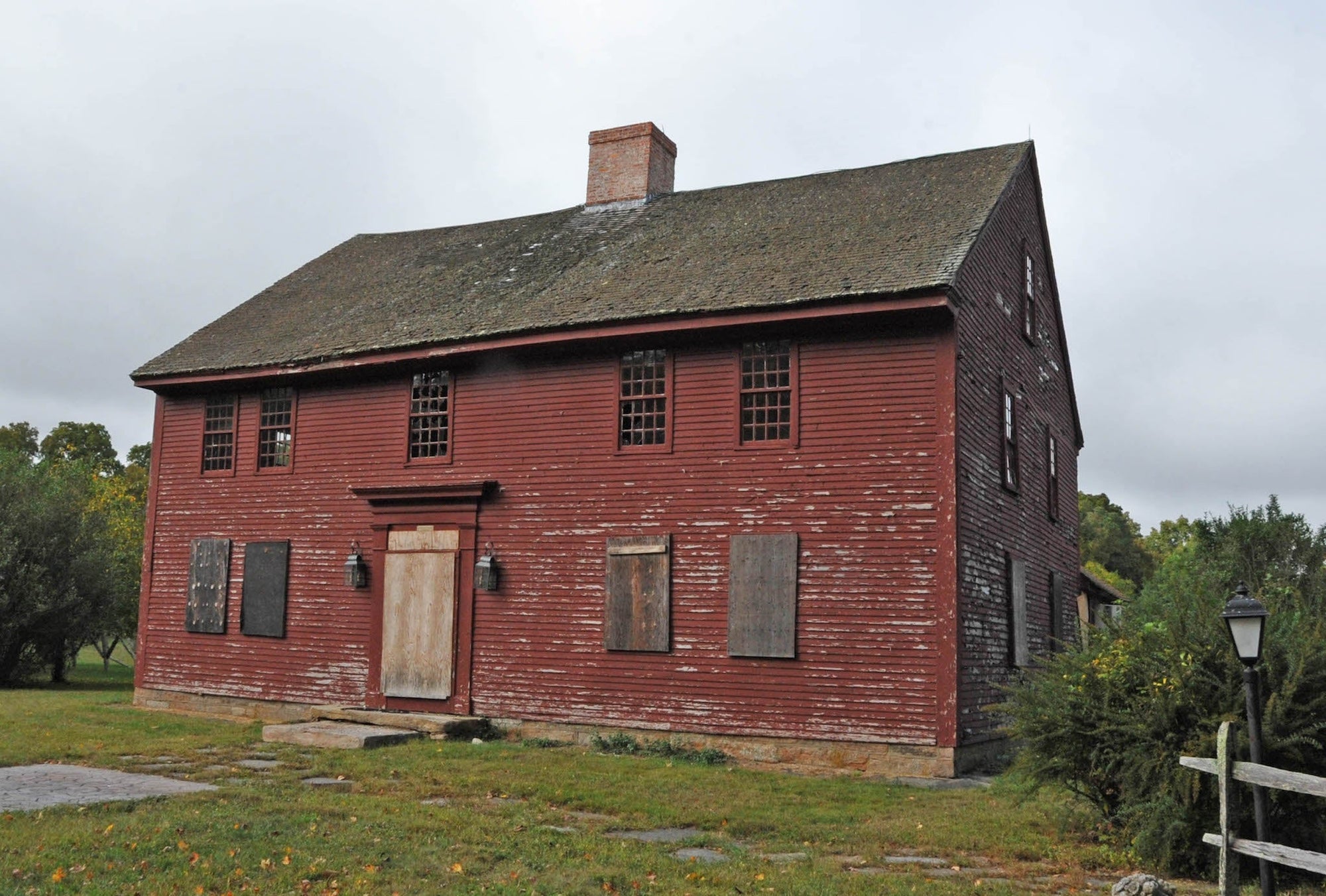 The John Randall House; a weathered two-story red wooden house with windows, a shingled roof and brick chimney