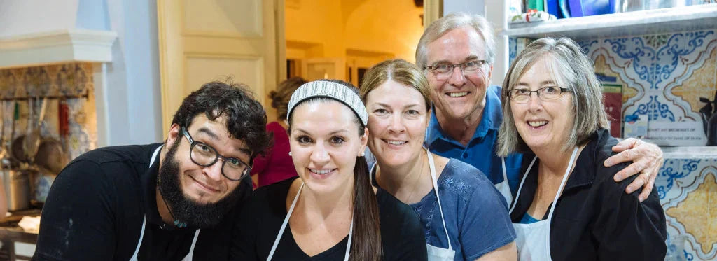 Five smiling people wearing aprons pose in a kitchen during a gluten free Italian pastry class