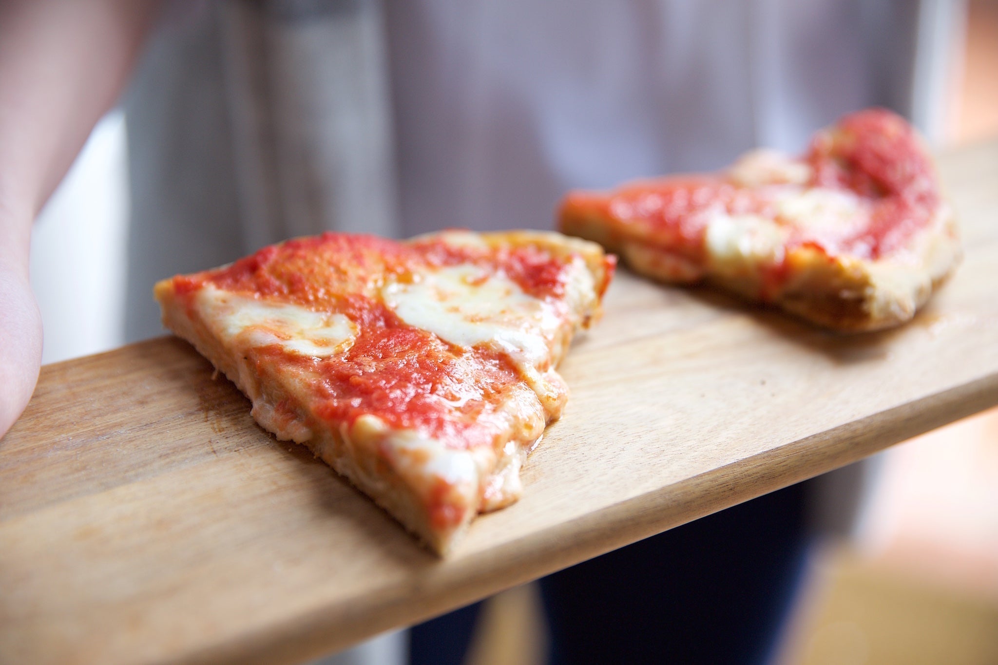 Two slices of Margherita pizza with tomato sauce and melted mozzarella on a wooden board held by a person