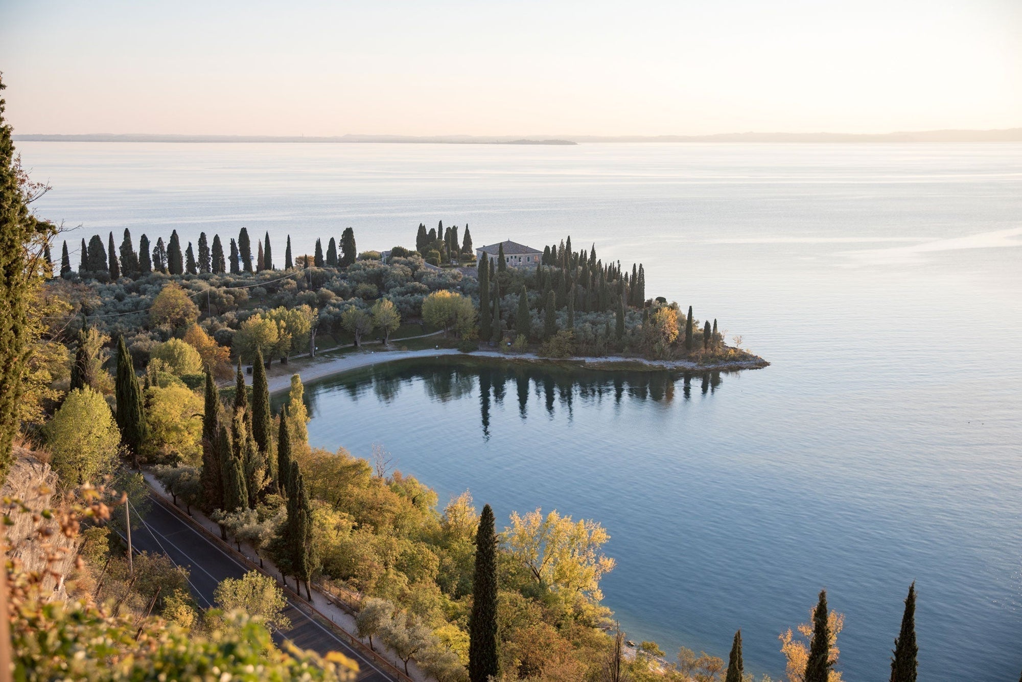  Peninsula at Lake Gada in Italy with cypress trees, olive groves and a villa reflected in calm blue water