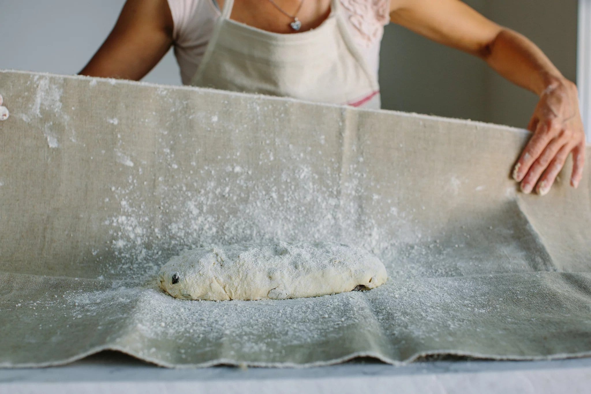 Hands of a baker folding a floured linen couche over a dusted loaf of dough