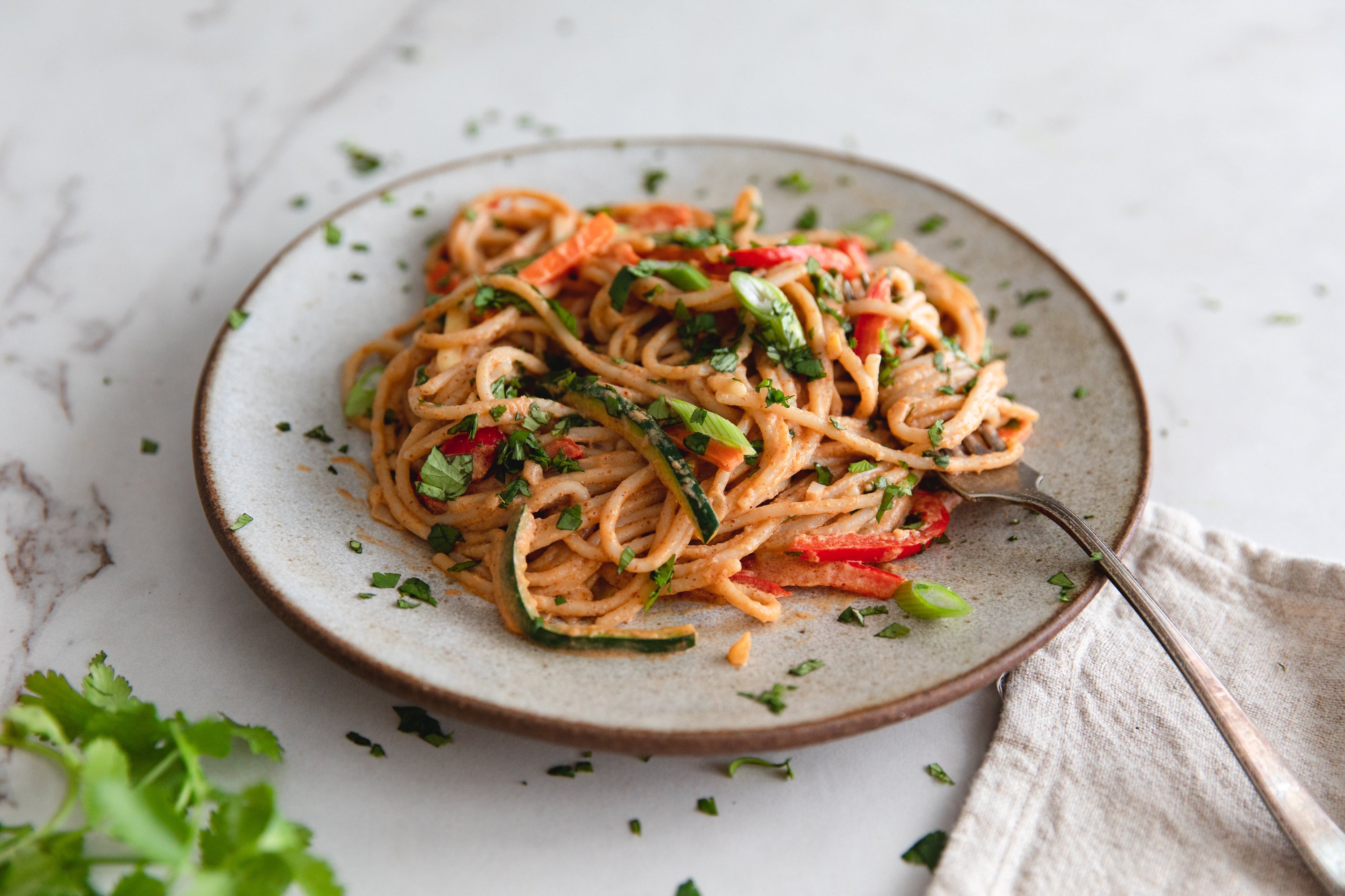 Zucchini noodle pasta with red pepper and chopped herbs on a ceramic plate with a fork