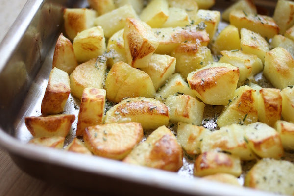 Close-up of rosemary and olive oil roasted potato wedges in a baking pan showing golden-brown crispy edges and scattered herbs