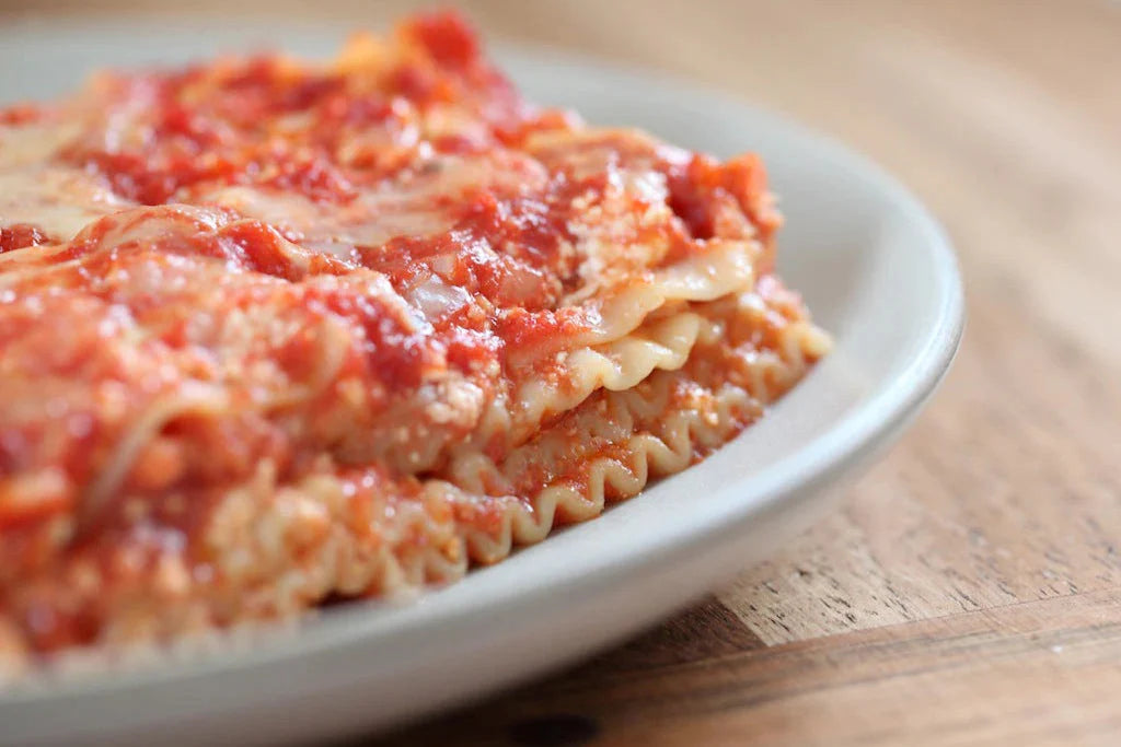 Side view of a gluten free lasagna slice showcasing layered ricotta, mozzarella, and tomato sauce on a white plate on a wooden table
