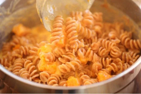 Stirring gluten-free fusilli pasta in a creamy butternut squash mac and cheese in a stainless-steel pot