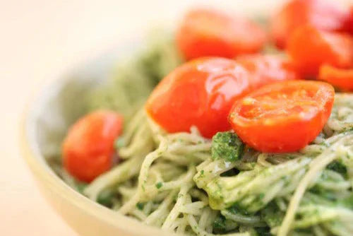 Close-up of capellini tossed in spinach pesto topped with roasted cherry tomatoes in a shallow bowl