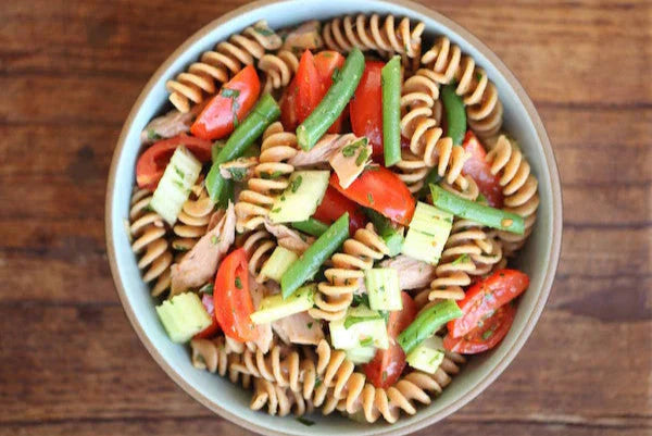 Bowl of Einkorn fusilli Nicoise-style pasta salad with tuna, green beans and cherry tomatoes on wooden table