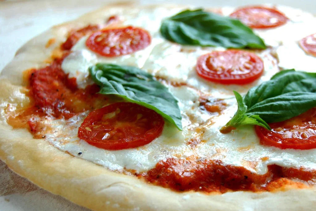 Close-up angled view of pizza made with Einkorn dough, showing melted mozzarella, tomato slices, and fresh basil on a wooden board