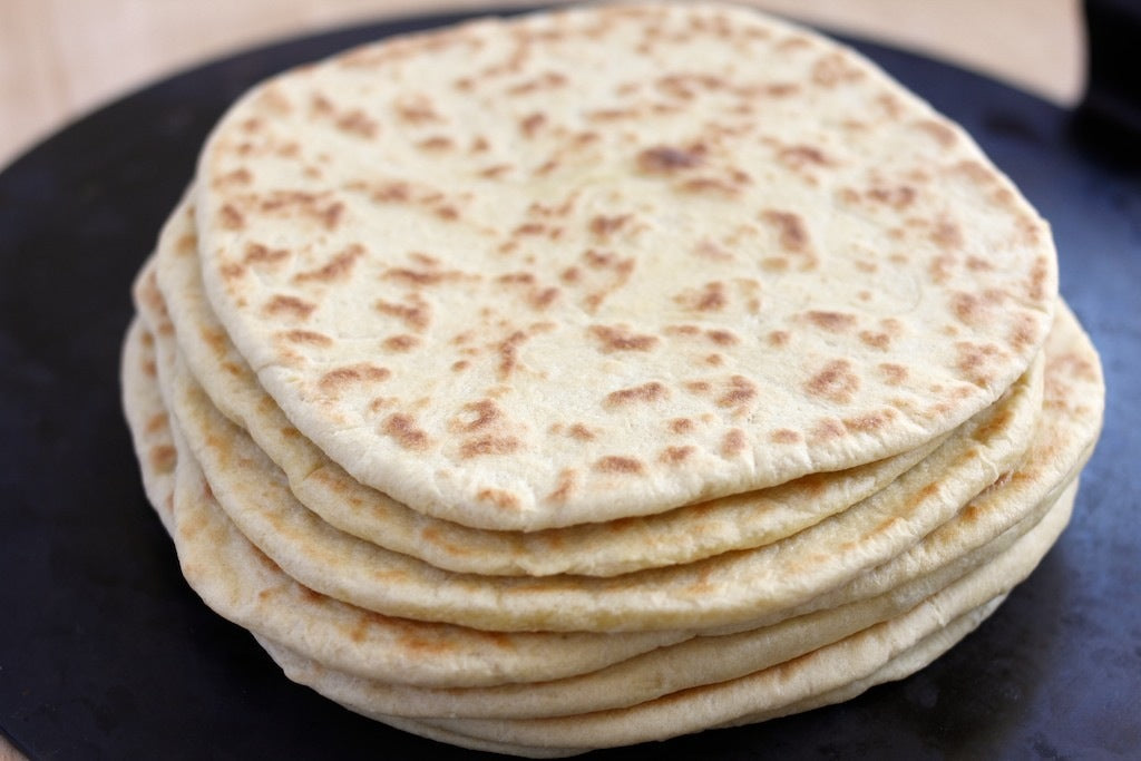 Close-up side view of stacked Italian piadina flatbreads showing golden-brown charred spots on a black griddle