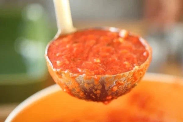 Ladle scooping organic tomato sauce from a pot in a home kitchen