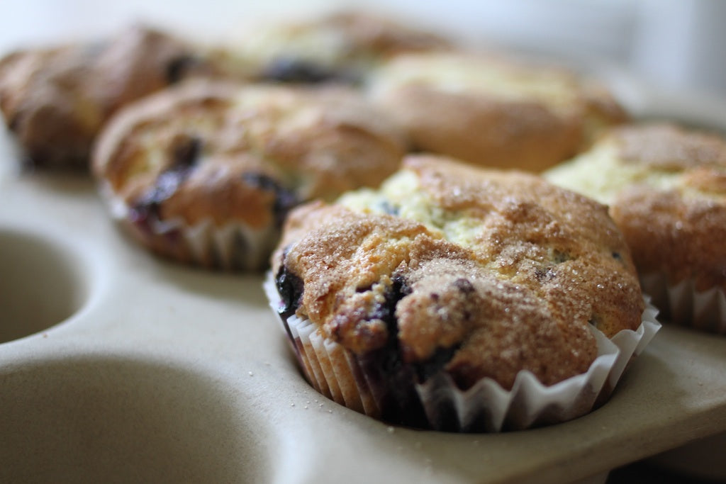 Close-up of a cinnamon-dusted einkorn blueberry muffin in a muffin tin showcasing sugared top and visible blueberries