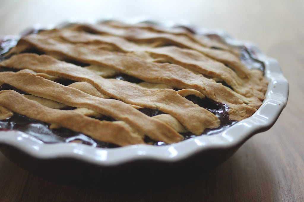 Close-up side view of lighter blueberry pie with golden lattice crust and glossy filling in a ceramic dish on a wooden table