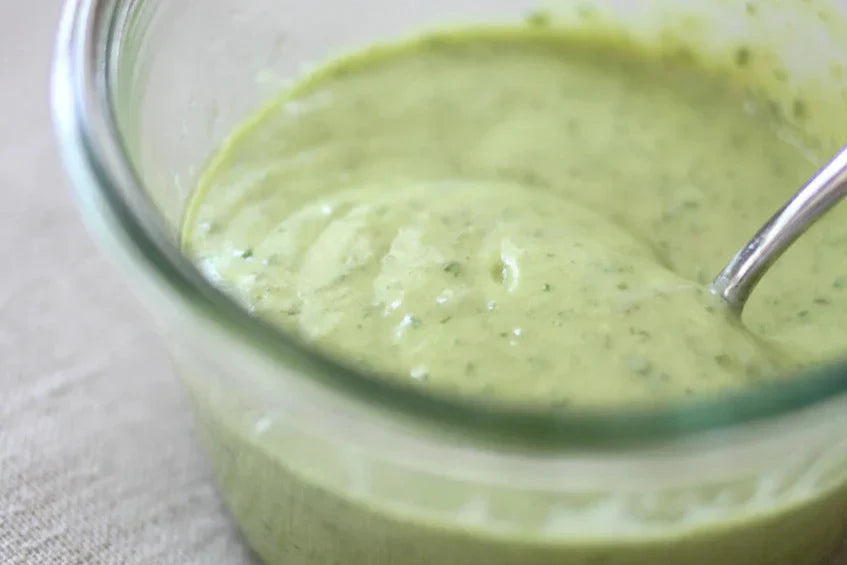 Close up of jar of organic Caesar dressing with creamy herb speckled texture and spoon on linen