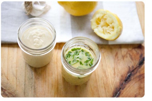 Two small jars of dressing, one garlic herb vinaigrette and one creamy dressing, on a wooden board with a halved lemon