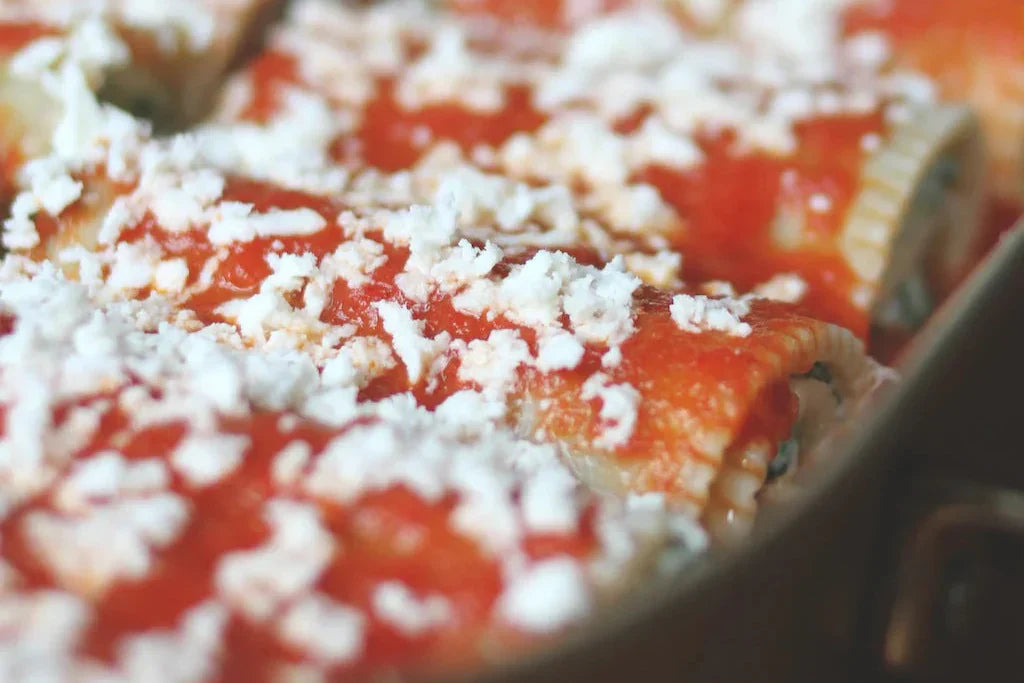 Baked gluten-free cannelloni in tomato sauce topped with crumbled cheese in a baking dish