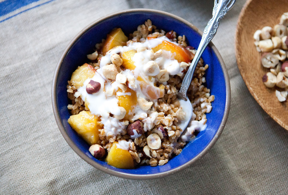 Caramelized peaches over einkorn wheat berries with yogurt and chopped hazelnuts in a blue bowl on a linen napkin