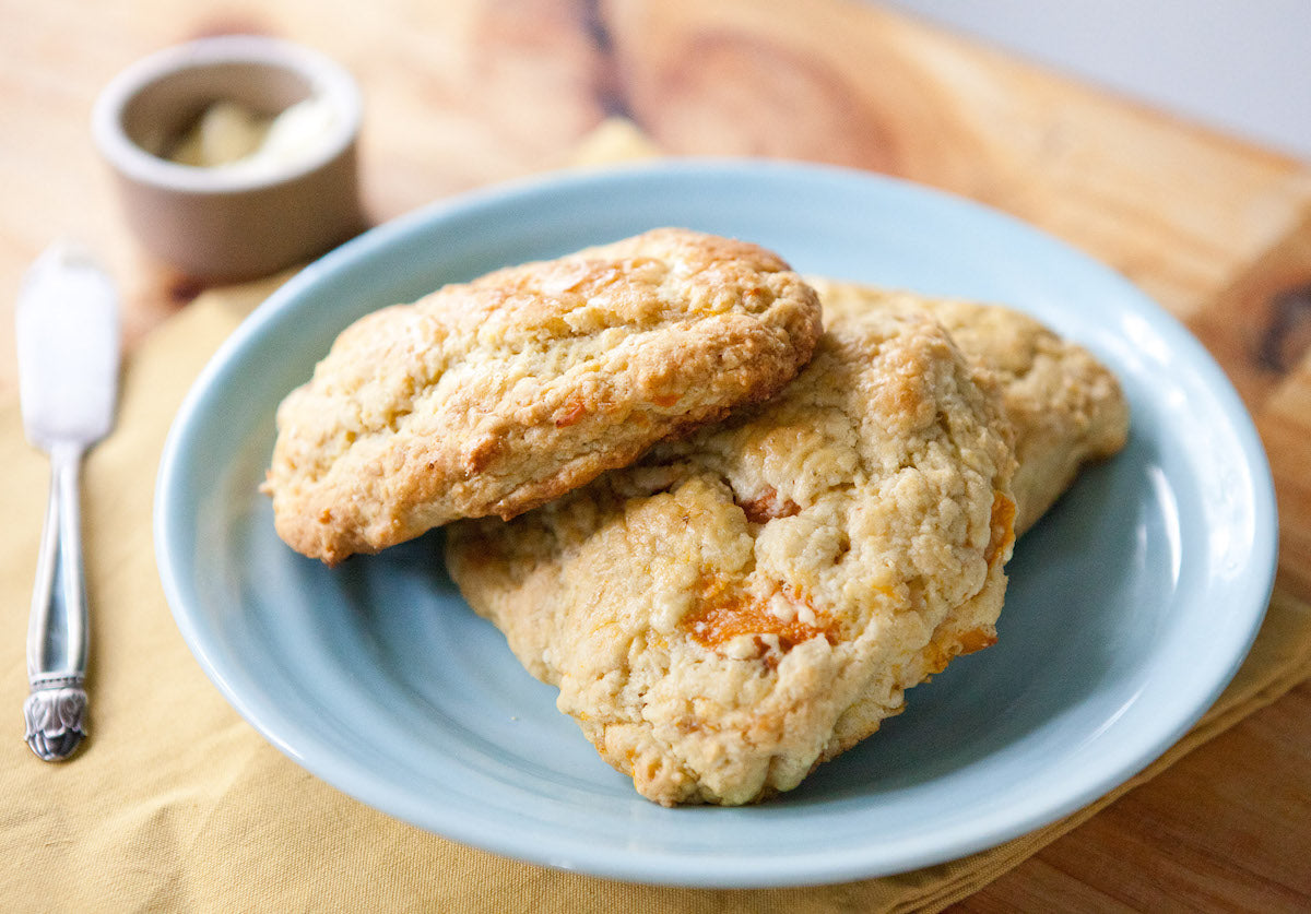 Close up of two einkorn ginger and apricot scones showing golden crumbly texture on a blue plate with a butter knife