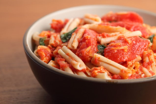 Close-up of Italian caserecce pasta tossed with garlicky tomato filets in a dark bowl on a wooden table
