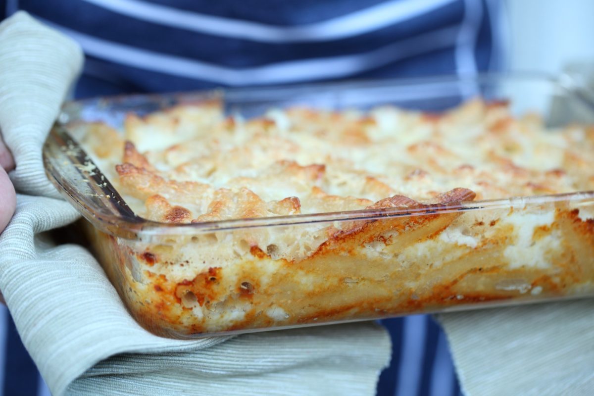 Close-up of a glass baking dish of gluten free baked macaroni and cheese with a golden-browned top held with a kitchen towel