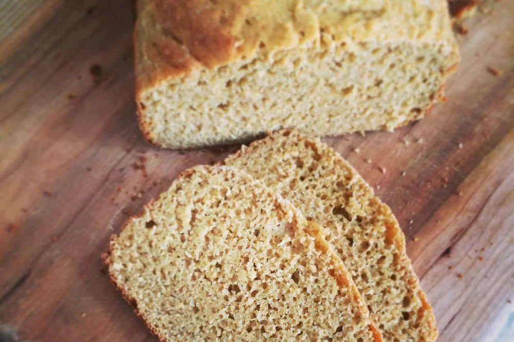 Two slices of 100% whole grain Einkorn bread with a partially sliced loaf on a wooden cutting board
