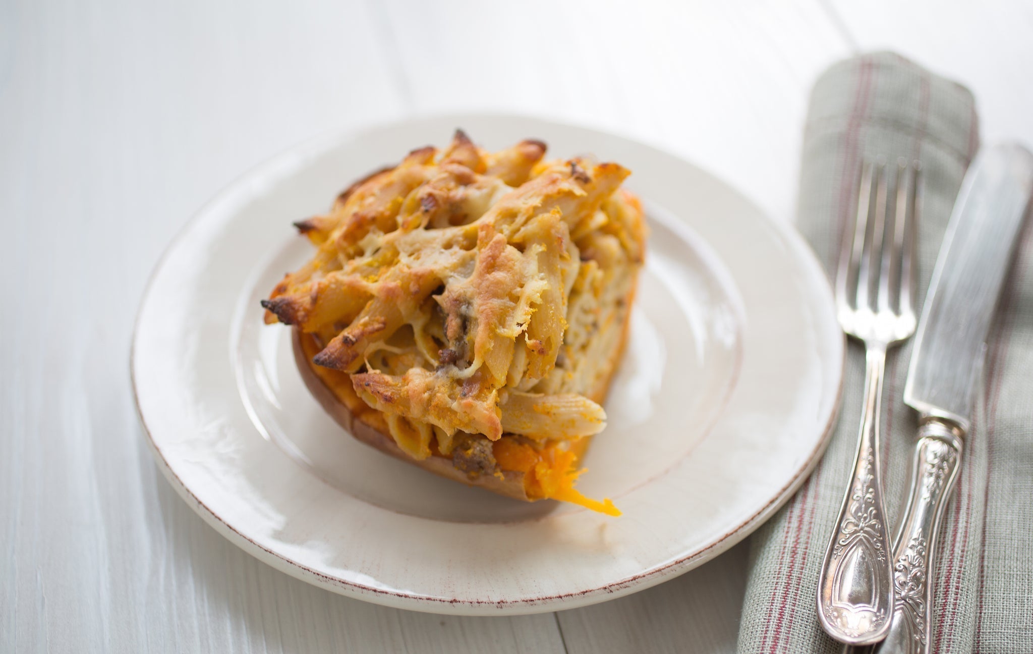 Pasta-stuffed roasted butternut squash half on a white plate with a fork and knife on a striped linen napkin