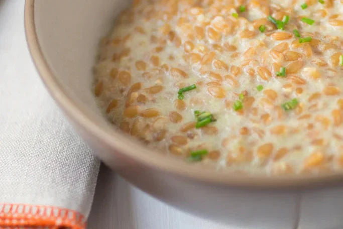 Close-up of Cream of Celery Einkorn Risotto showing creamy texture, whole einkorn grains and chives in a beige bowl with a folded linen napkin